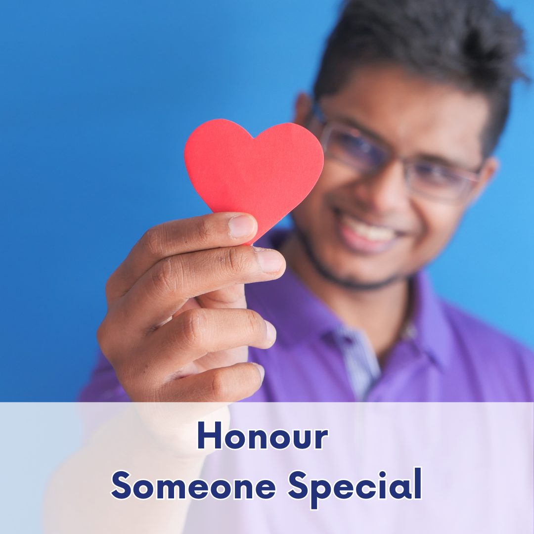 Person smiling while holding a small red heart in their hand, symbolizing appreciation, gratitude, and giving in honour of someone meaningful.